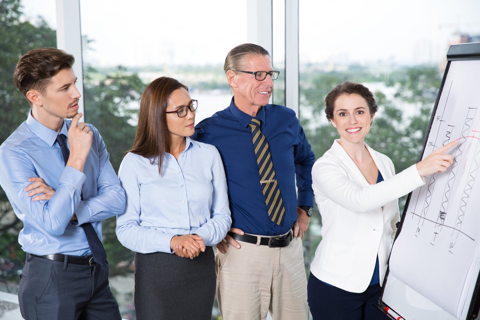 Happy businesswoman presenting bar chart on whiteboard to her concentrated colleagues at meeting in conference room